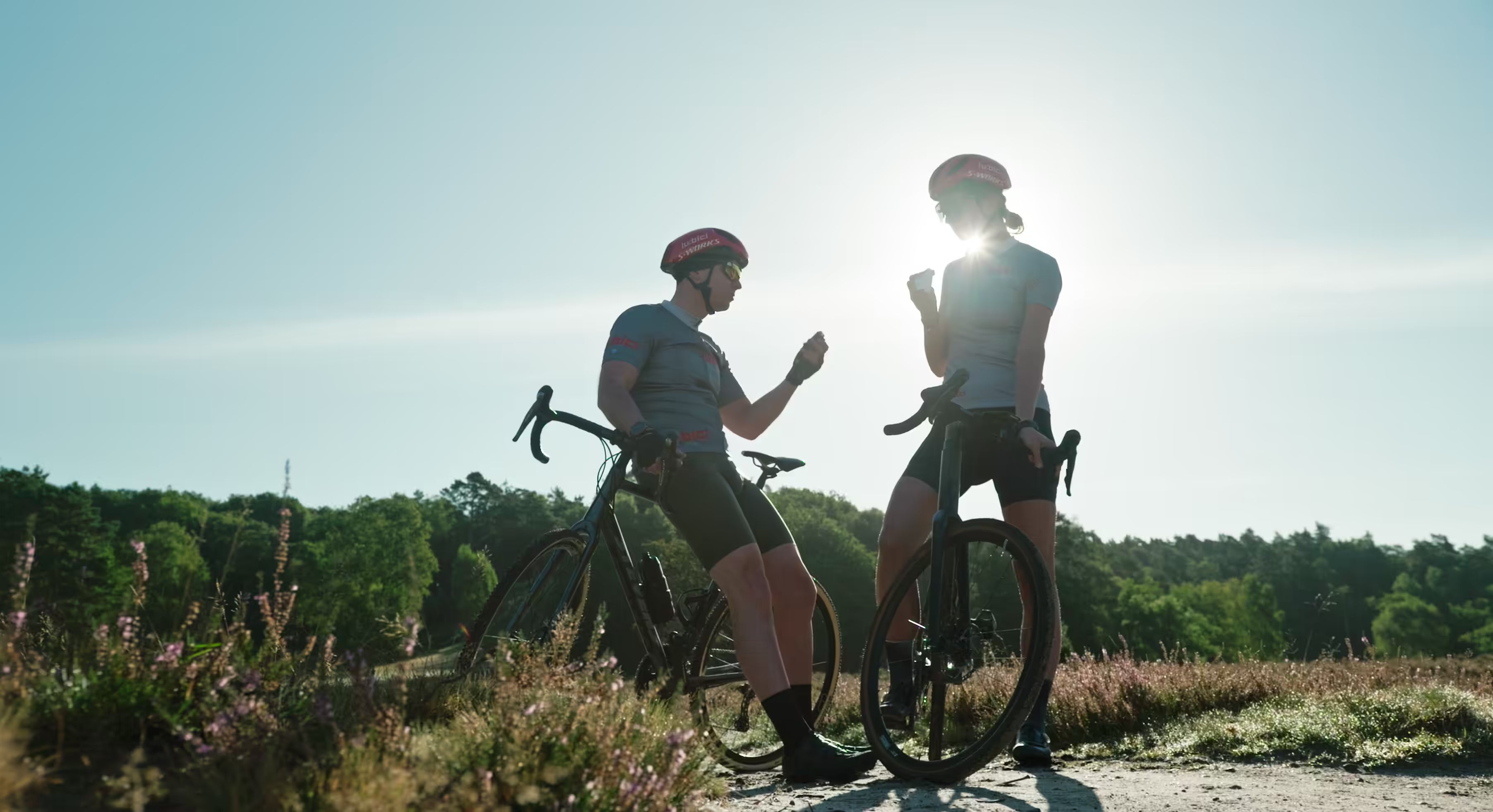 Ein Radfahrer und eine Radfahrerin machen auf ihren Fahrrädern Pause und essen einen Fitnessriegel.